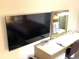 Habitación de hotel con televisión de pantalla plana montada en la pared, tocador con espejo y teléfono, y escritorio con silla.