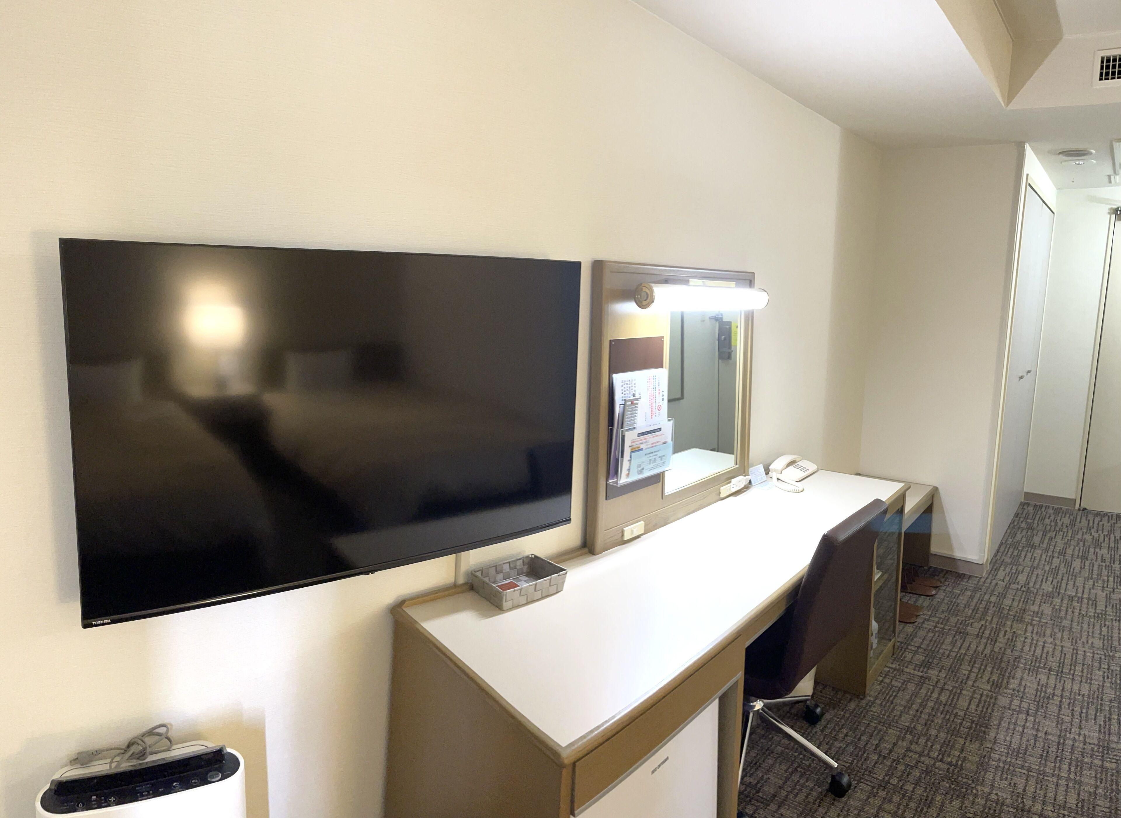 Habitación de hotel con televisión de pantalla plana, escritorio con espejo, teléfono y piso cubierto de alfombra.