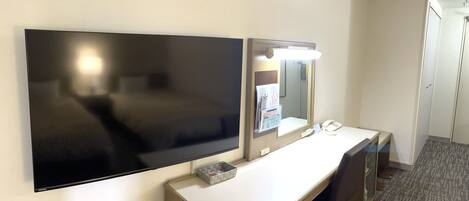 Habitación de hotel con televisión de pantalla plana, escritorio con espejo, teléfono y piso cubierto de alfombra.