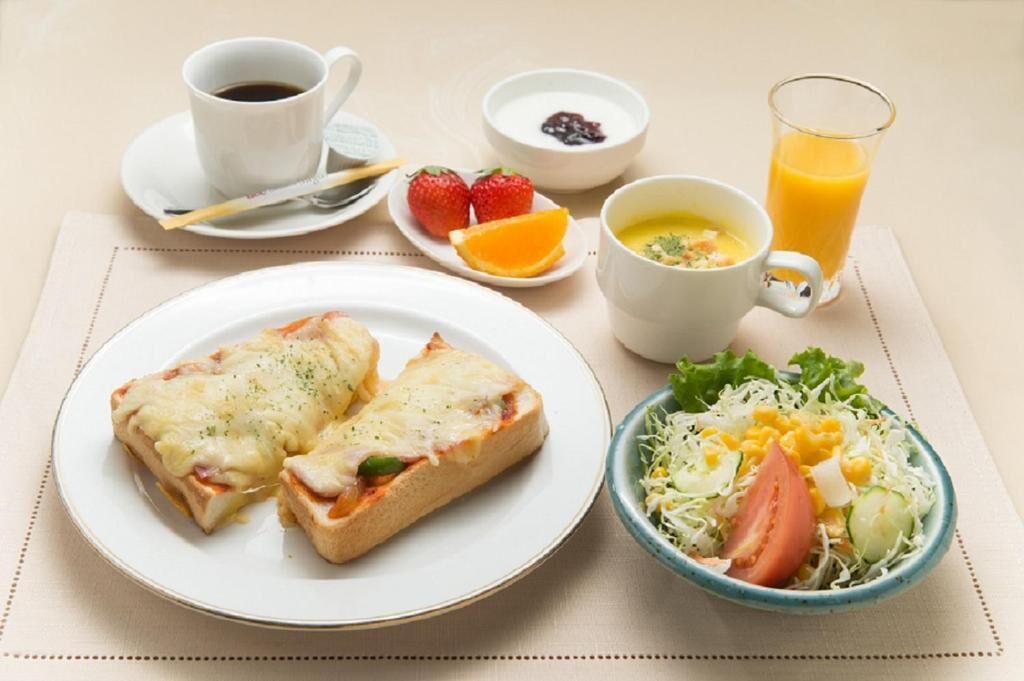 Uma mesa de café da manhã com torradas, café, frutas, sopa e salada.