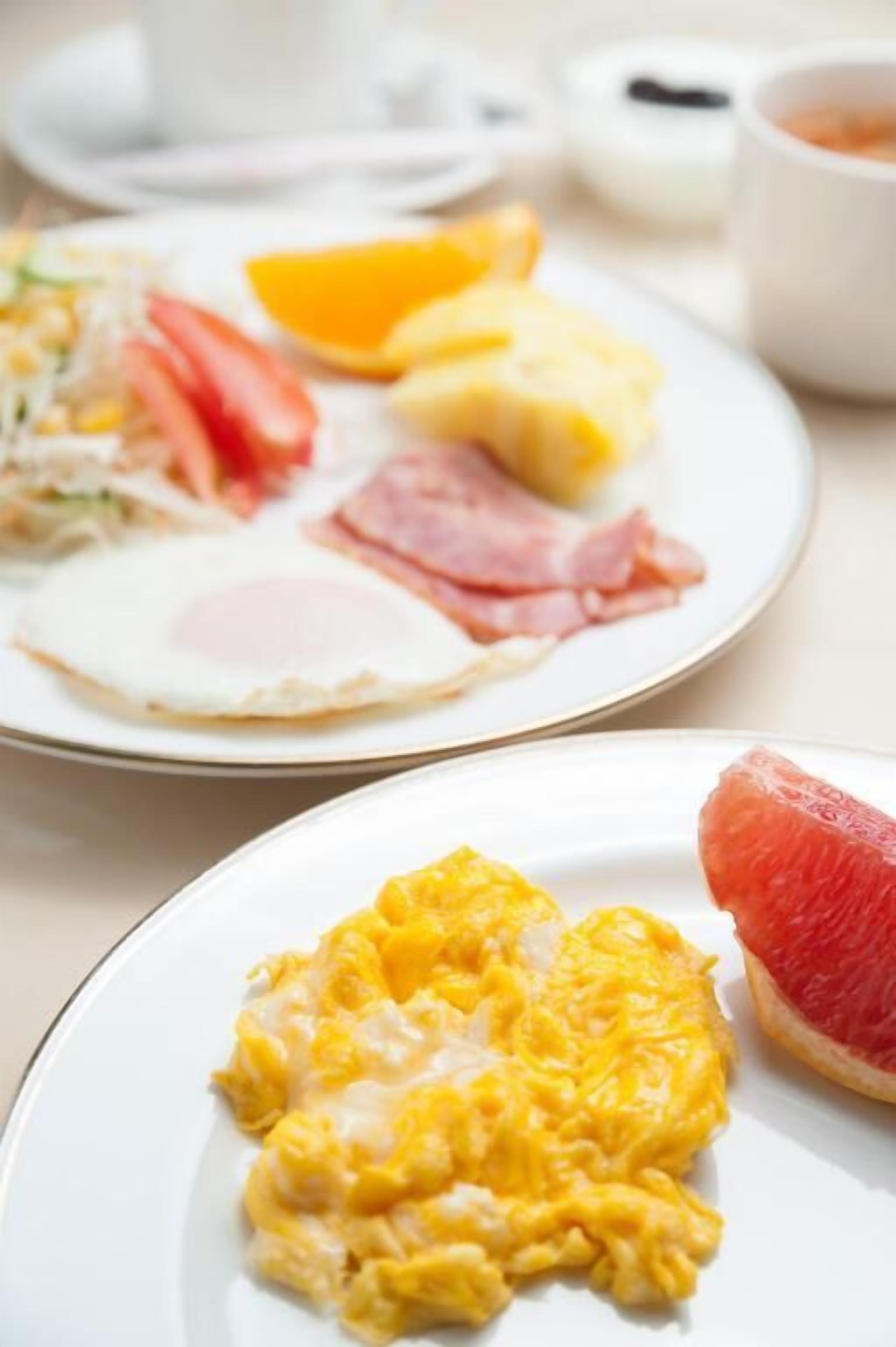 Ein Frühstücksteller mit Rührei, Speck, Tomaten und Orangenscheiben.