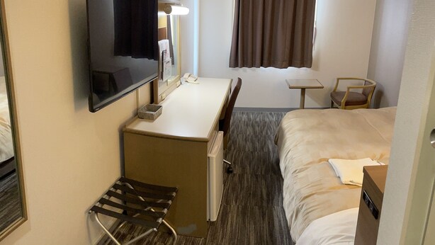 A hotel room with a bed, a desk with a chair, a TV, a small table, a chair, a mirror, and a window with curtains. - Hotel Yassa (Mihara)