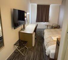 Habitación de hotel con cama, escritorio con silla, televisión, mesita, sillón y ventana con cortinas.