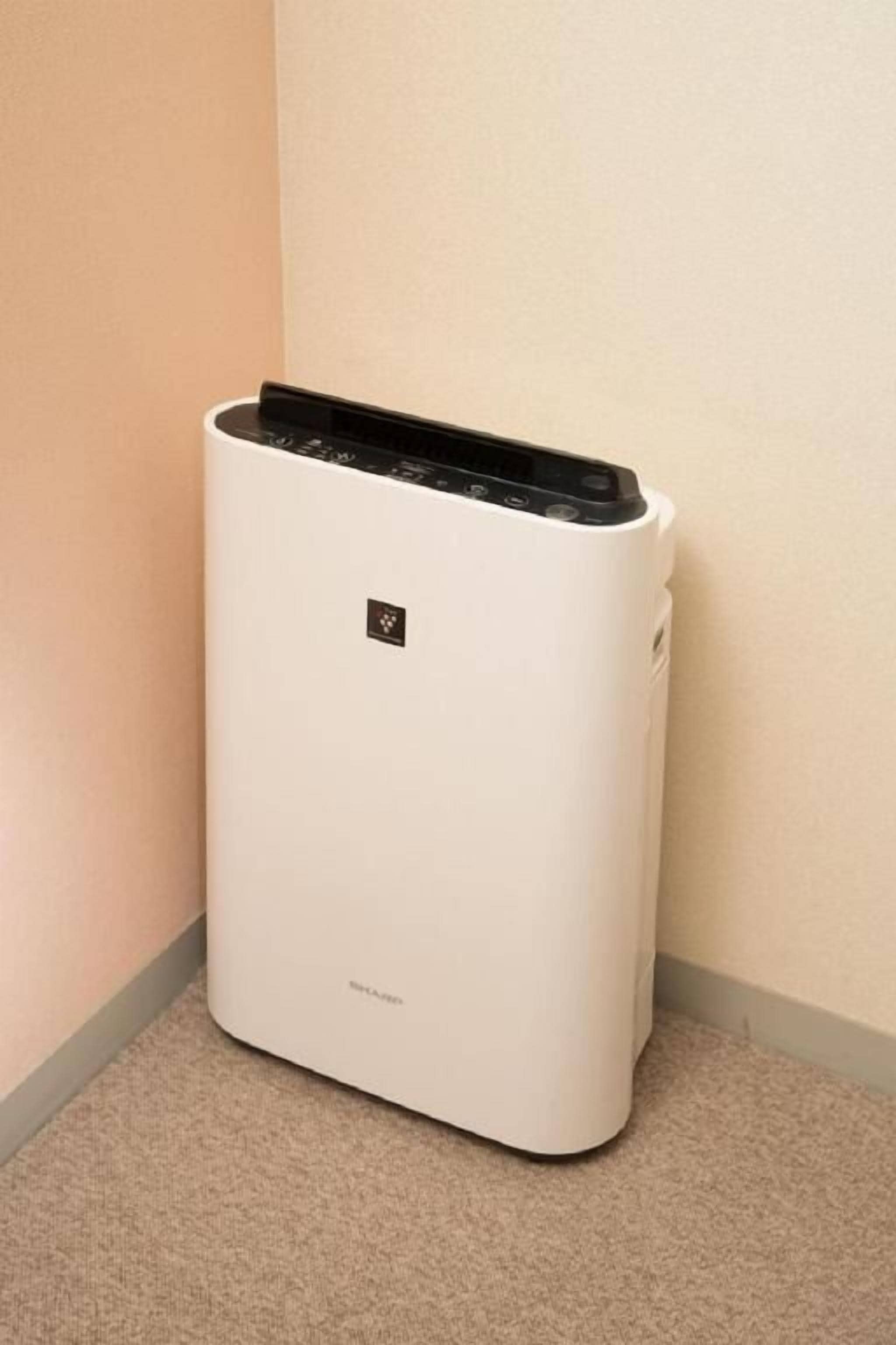 Een witte, verplaatsbare airconditioner in een hoek van een kamer met een beigekleurig tapijt en muren.