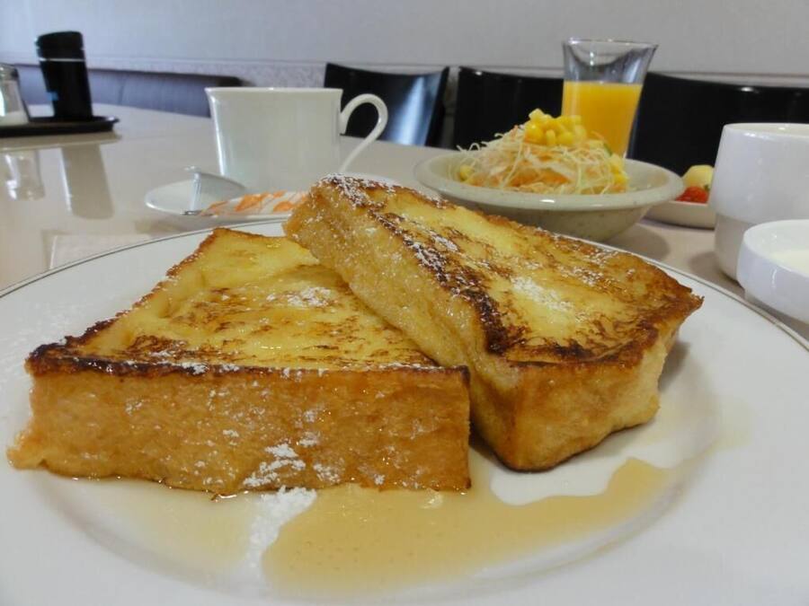 A breakfast plate with French toast, syrup, and a side of fruit salad.