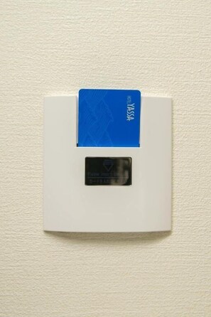 A white wall-mounted device with a blue card on top and a black label below. - Hotel Yassa (Mihara)