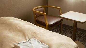 A hotel room with a bed, a wooden chair, a small table, and a window with curtains.