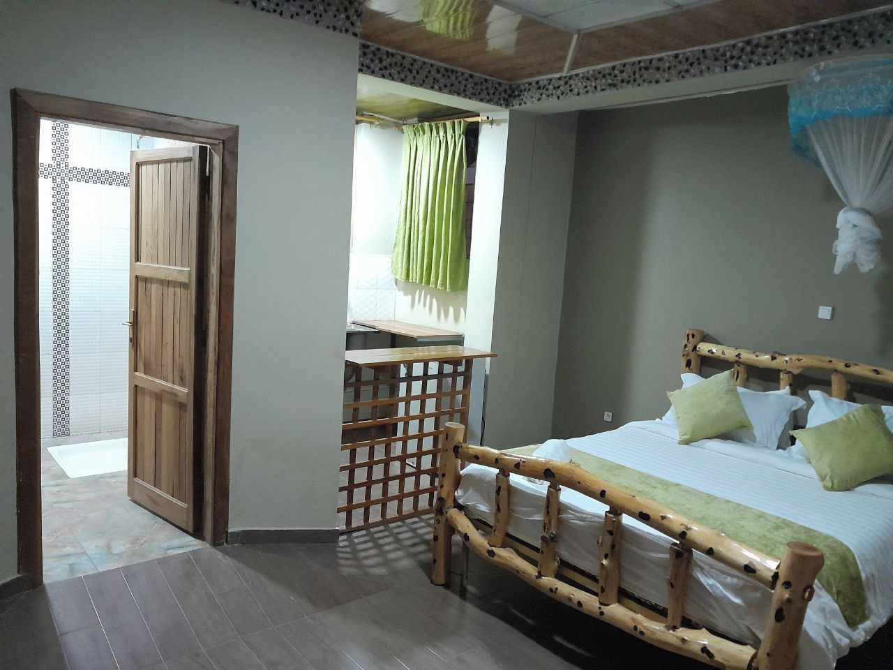 A room with a wooden bed, a window with a green curtain, and a wooden partition.