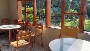 A room with a round table and wooden chairs, large windows with a view of a garden.