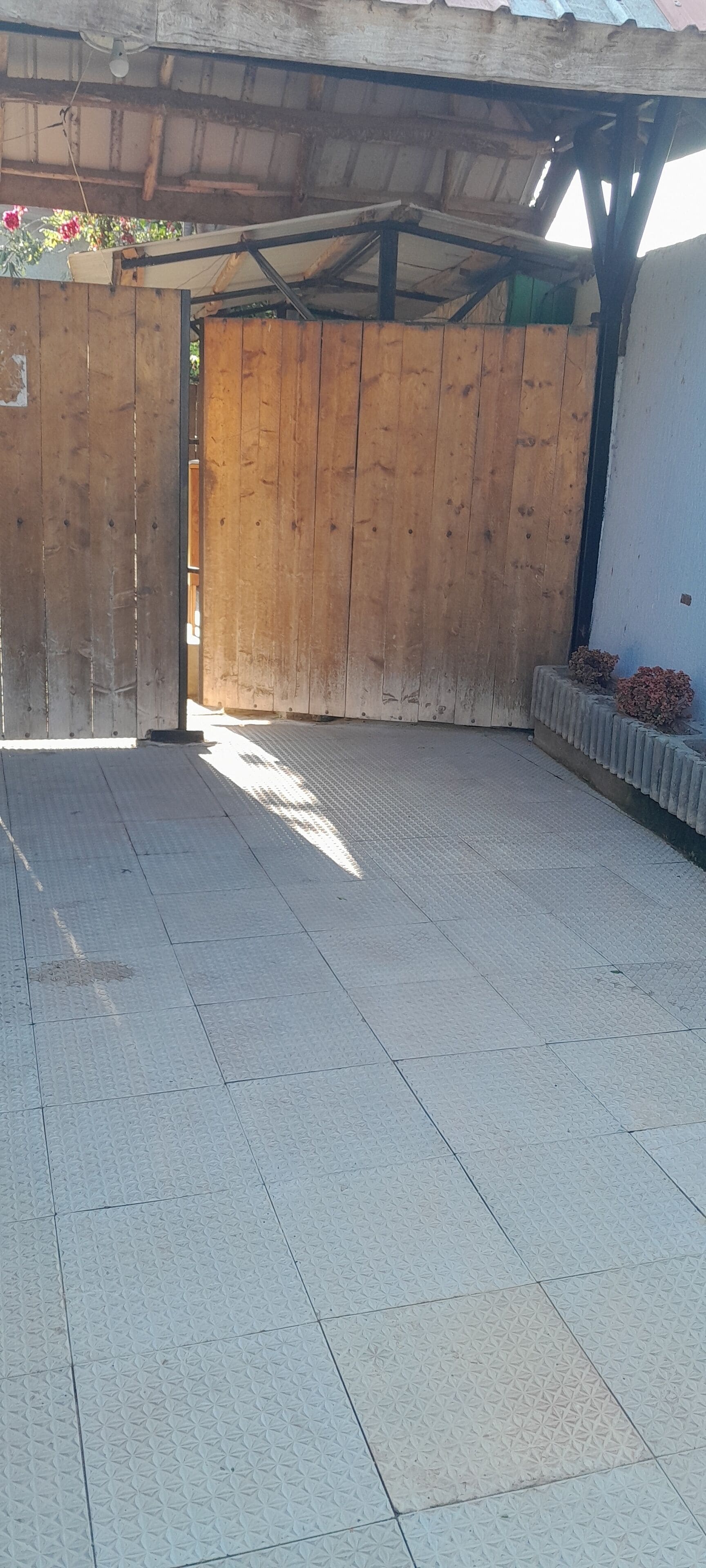 Área externa coberta com cerca de madeira, piso de azulejos e um banco de concreto.