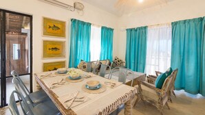 A dining area with a table set for four, chairs, and a ceiling light fixture. - Beach front villa Myconos (Anjuna)