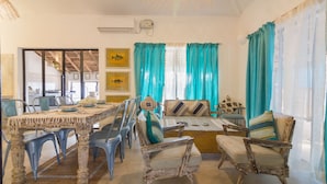 A dining area with a rustic wooden table, blue chairs, and a sofa with patterned cushions. - Beach front villa Myconos (Anjuna)