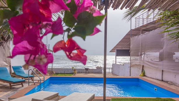 A pool area with lounge chairs, a view of the ocean, and a covered structure. - Beach front villa Myconos (Anjuna)