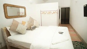 A bedroom with a bed, pillows, a bedside table, a mirror, and a wardrobe. - Beach front villa Myconos (Anjuna)