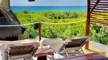 Relax in a tranquil ocean-view seating area with lounge chairs and a wooden table, shaded by a pergola with a thatched roof.