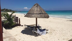 Una playa con una sombrilla de paja, sillas de descanso y una palmera.