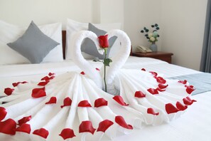 Un lit avec du linge de lit blanc, une disposition de serviettes en forme de cœur et des pétales de rose éparpillés.