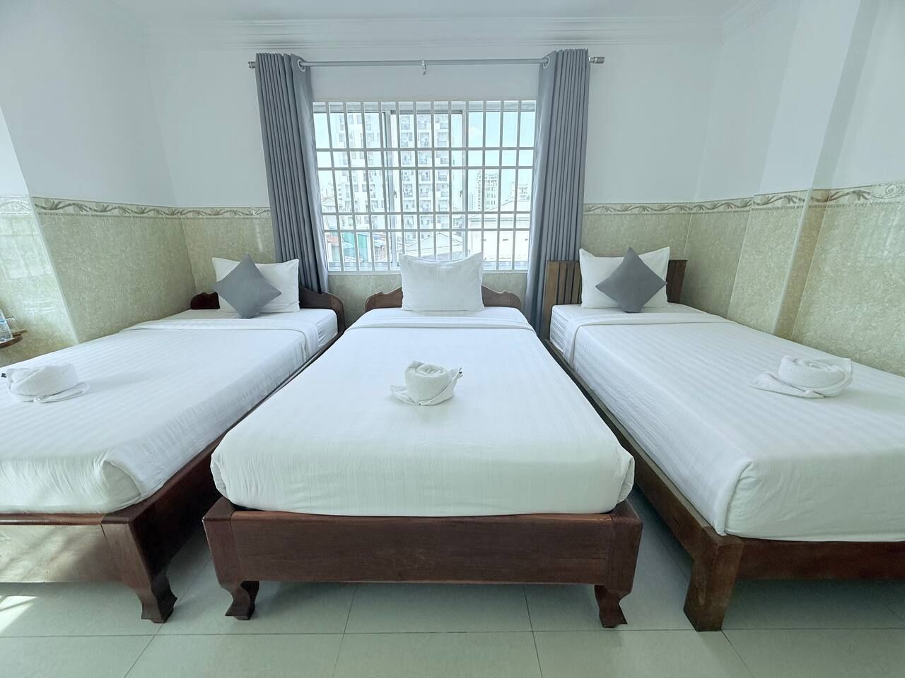 A hotel room with three single beds, a large window with curtains, and a view of buildings outside.