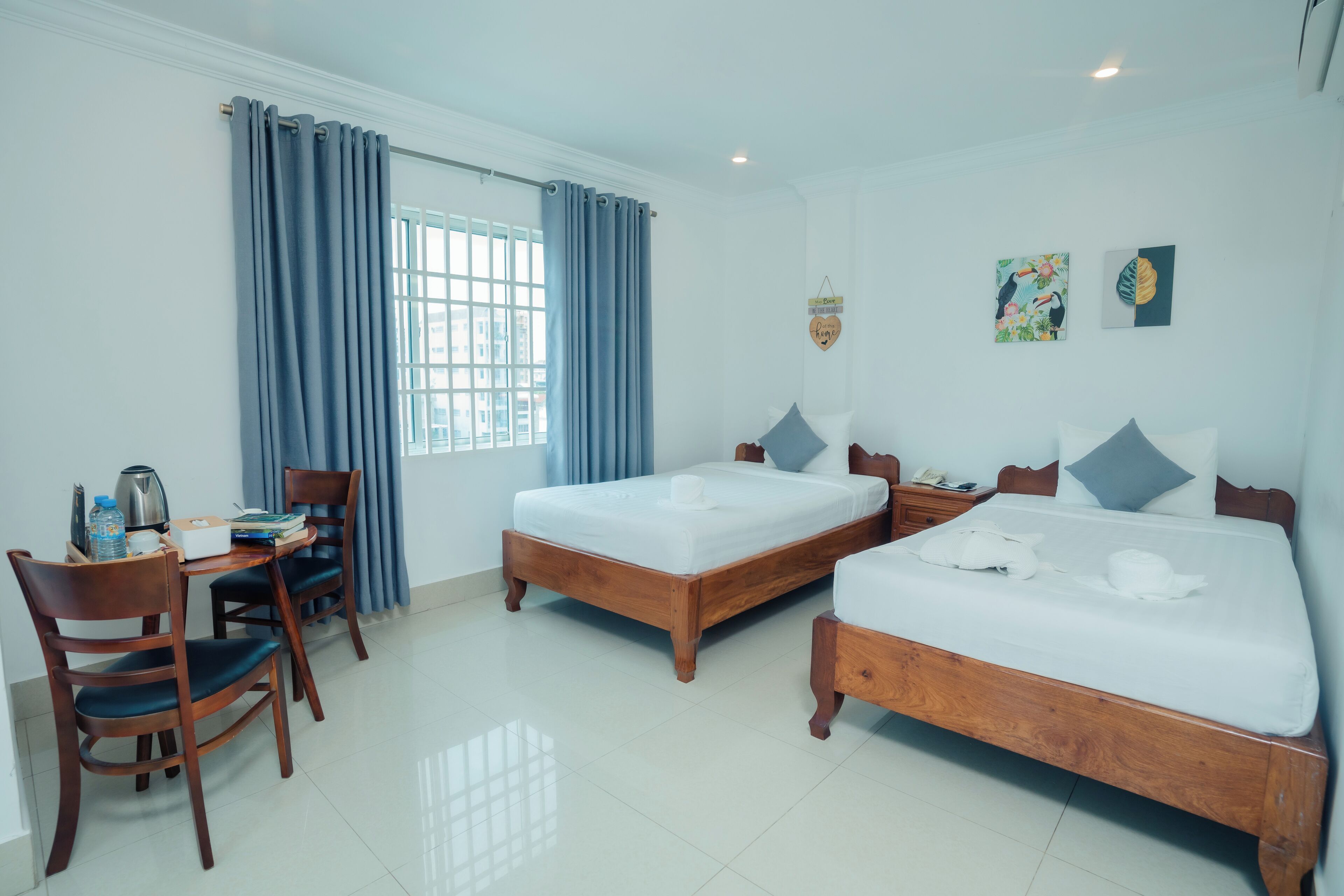 A hotel room with two wooden beds, a desk with chairs, a window with curtains, and wall art.