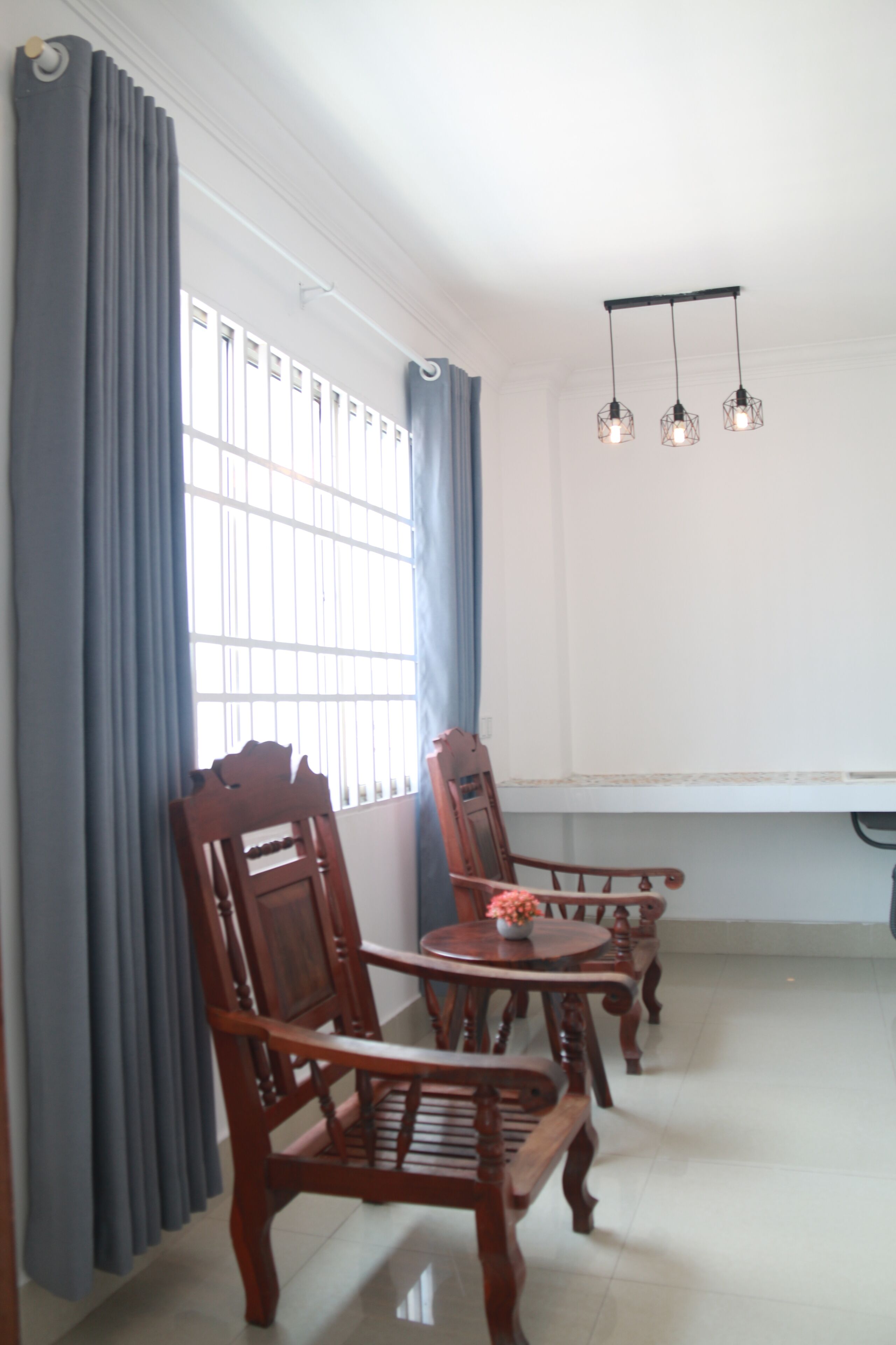 Un comedor con una mesa y cuatro sillas de madera, una ventana con cortinas azules y una lámpara colgante.