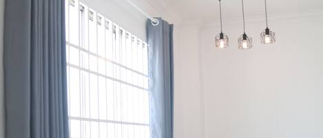 Un comedor con una mesa y cuatro sillas de madera, una ventana con cortinas azules y una lámpara colgante.