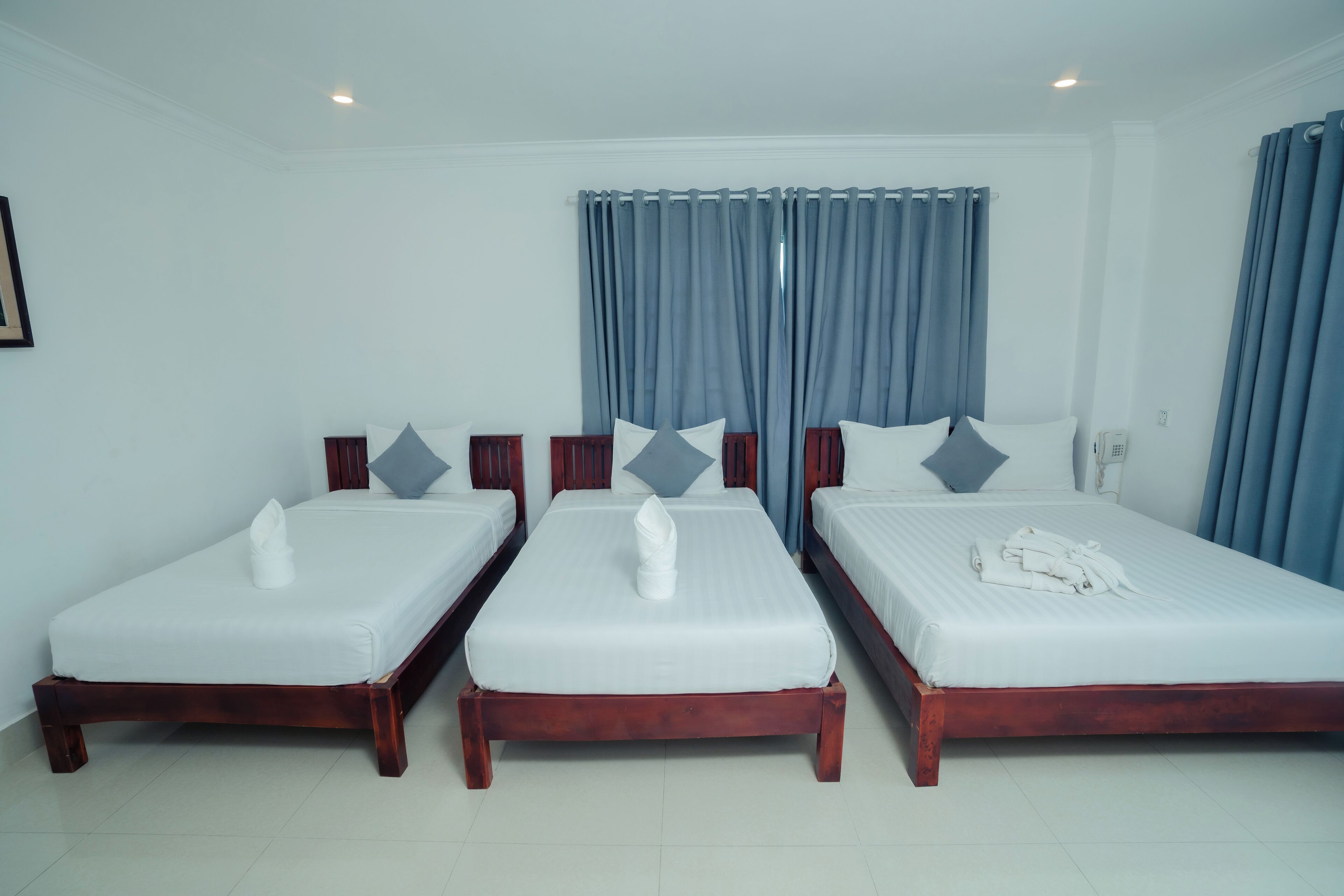 Una habitación de hotel con tres camas individuales, cada una con colchón blanco y cabecero de madera.