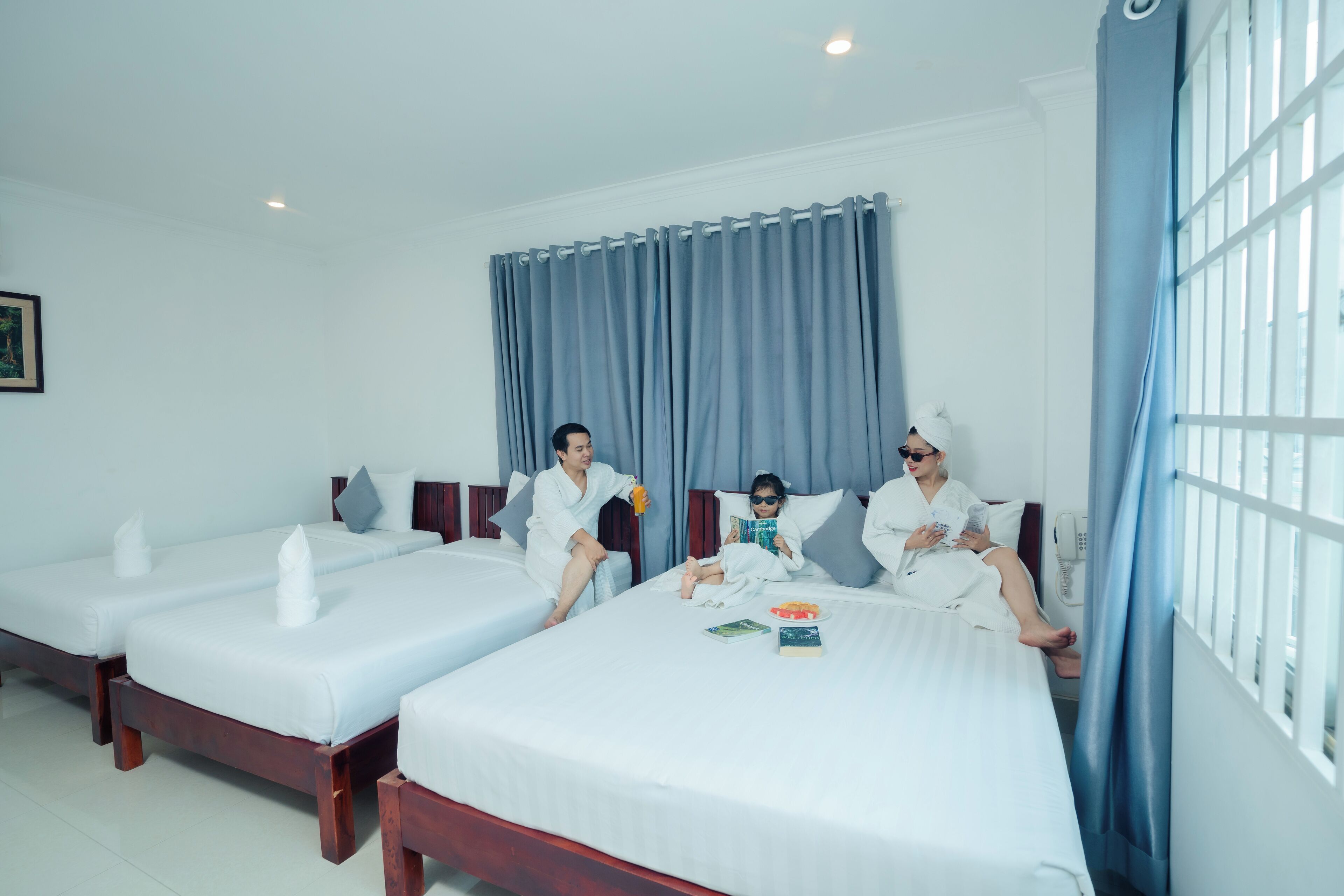 A hotel room with two single beds, a large window with blue curtains, and a white wall.