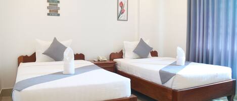 Habitación de hotel con dos camas de madera, ropa blanca y almohadas grises. Se observa un cuadro en la pared y una cortina en la ventana.