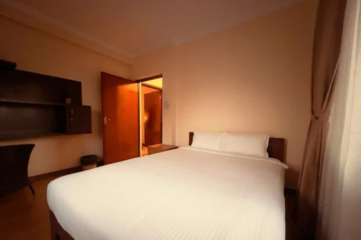 A hotel room with a large bed, a desk, and a wardrobe.