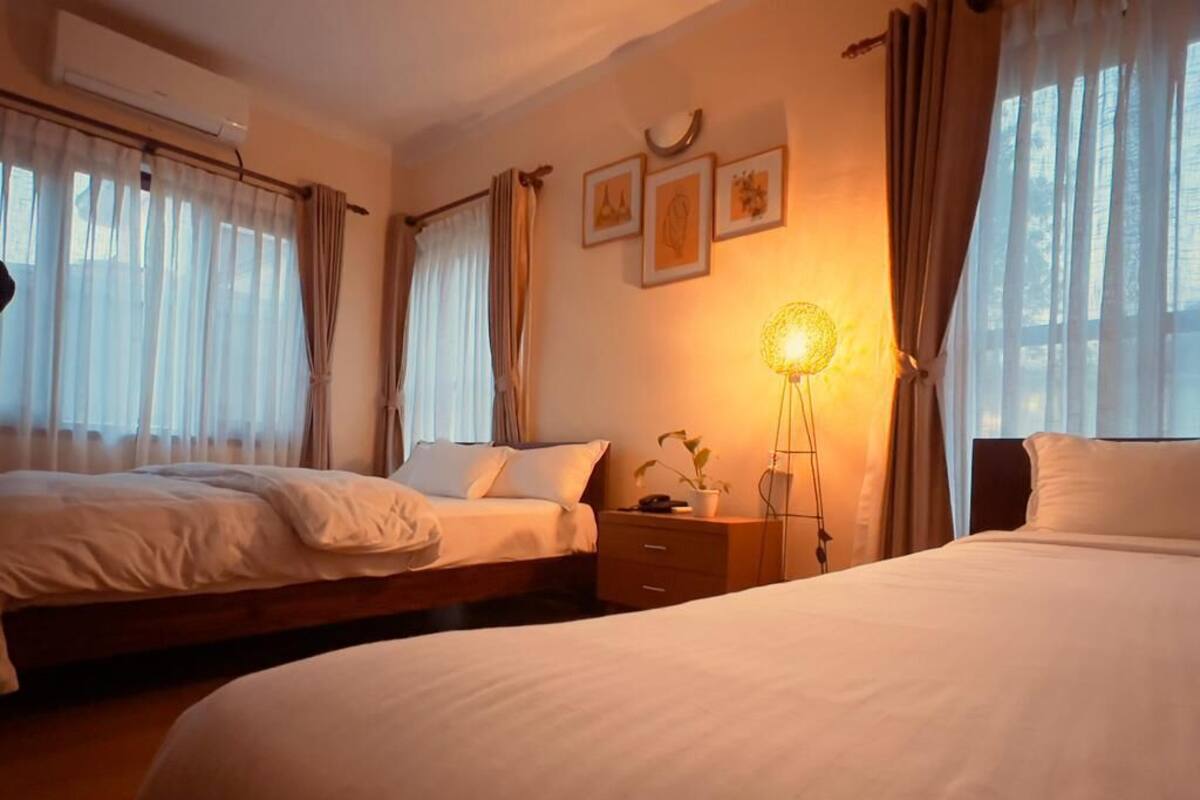 A hotel room with two beds, a bedside table with a lamp, and a wall-mounted clock.