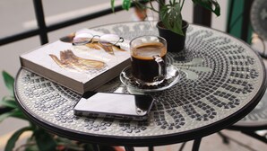 Ein runder Tisch aus Metall mit einer Kaffeetasse, einem Buch und einer Brille.