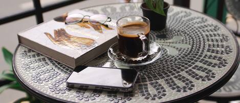A round metal table with a glass of coffee, a book, and a pair of glasses.