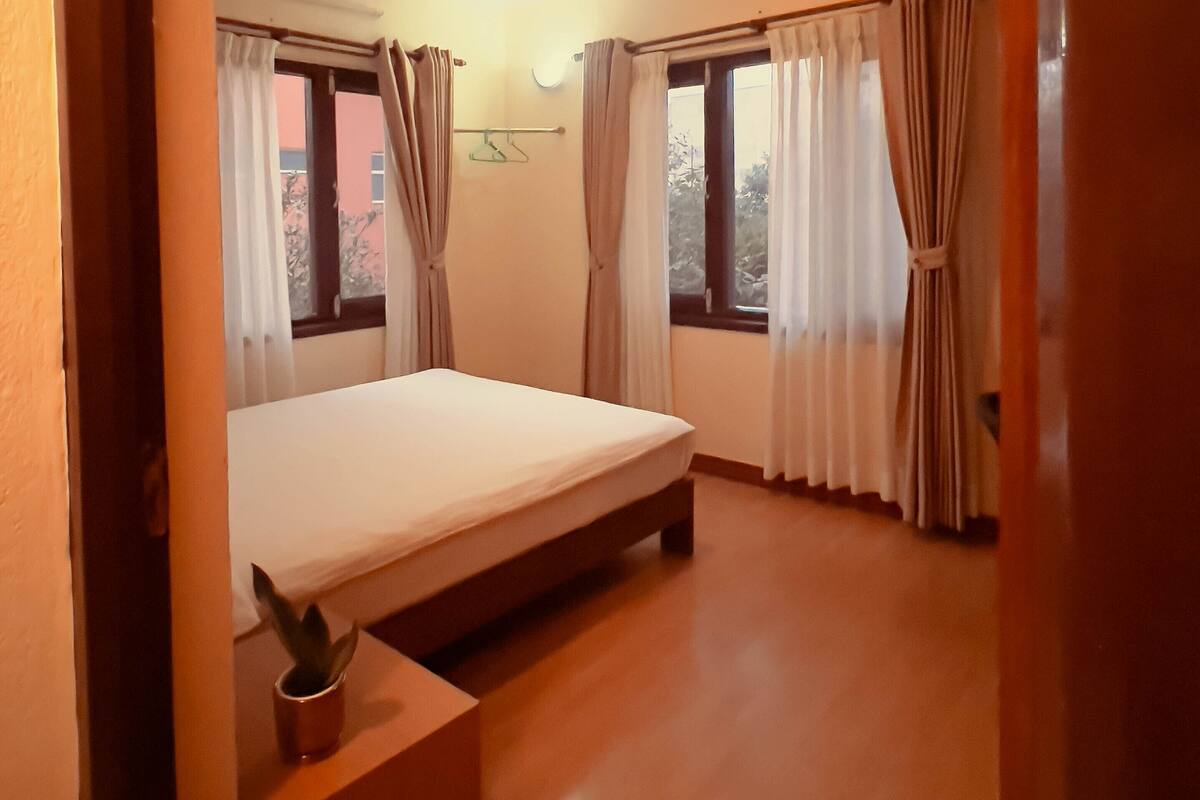 A bedroom with a bed, a bedside table with a plant, and a window with curtains.