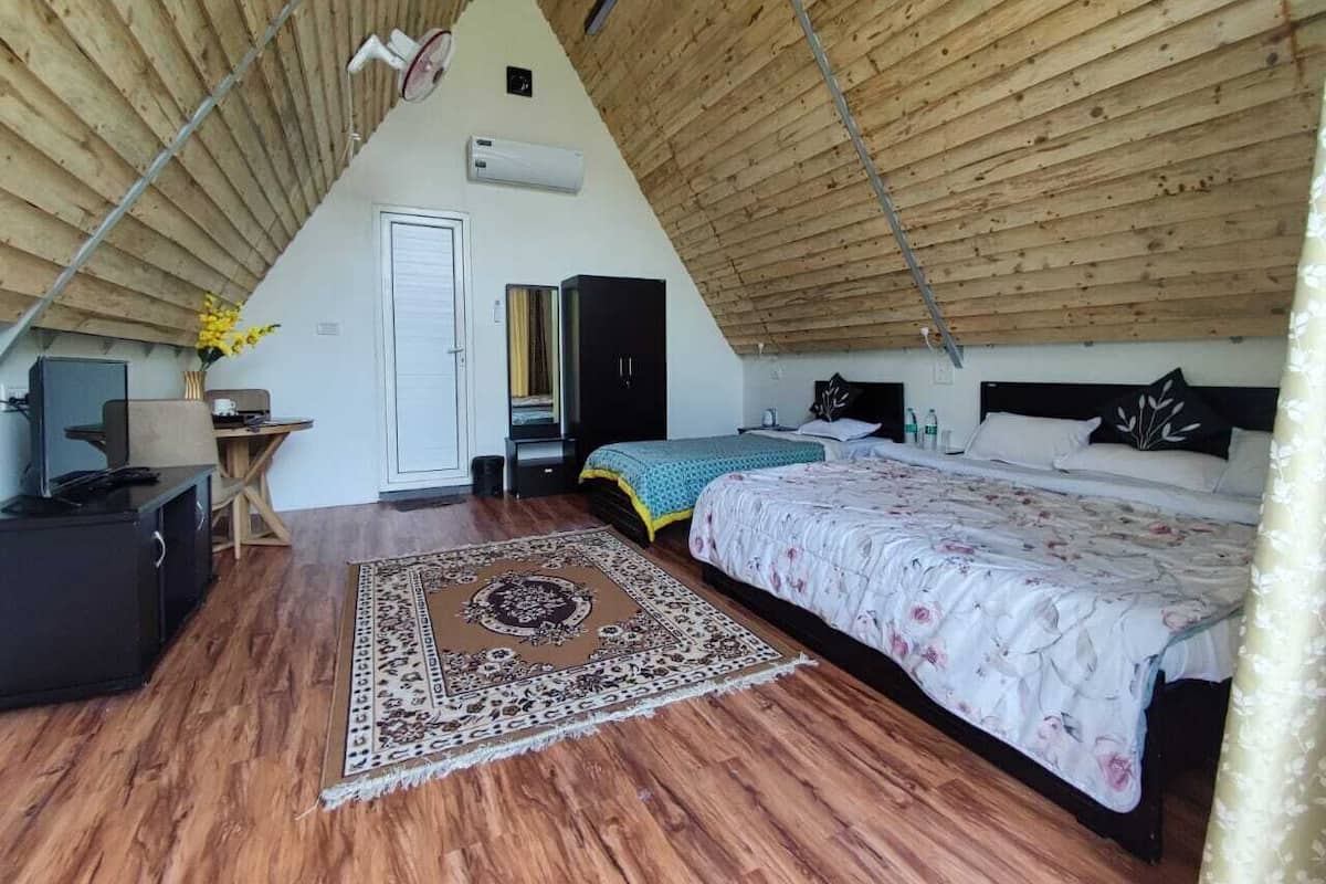 A bedroom with a sloped ceiling, a bed, a desk, a chair, and a small table with a vase of flowers.