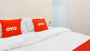 A bed with white bedding and two red pillows with the word "OYO" on them.