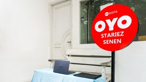 A white door, a red sign with "OYO STARIEZ SENEN" text, a blue table with a laptop, and a black folder.