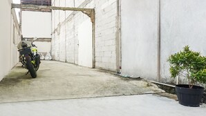 A narrow alleyway with a motorcycle parked on the left, a satellite dish on the wall, and a potted plant on the right.