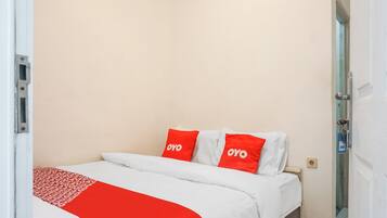 Une chambre d’hôtel avec un lit, du linge de lit blanc et des oreillers rouges sur lesquels est inscrit le mot « OYO ».