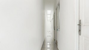 A long, narrow hallway with white walls and a shiny tiled floor, leading to a set of closed doors.