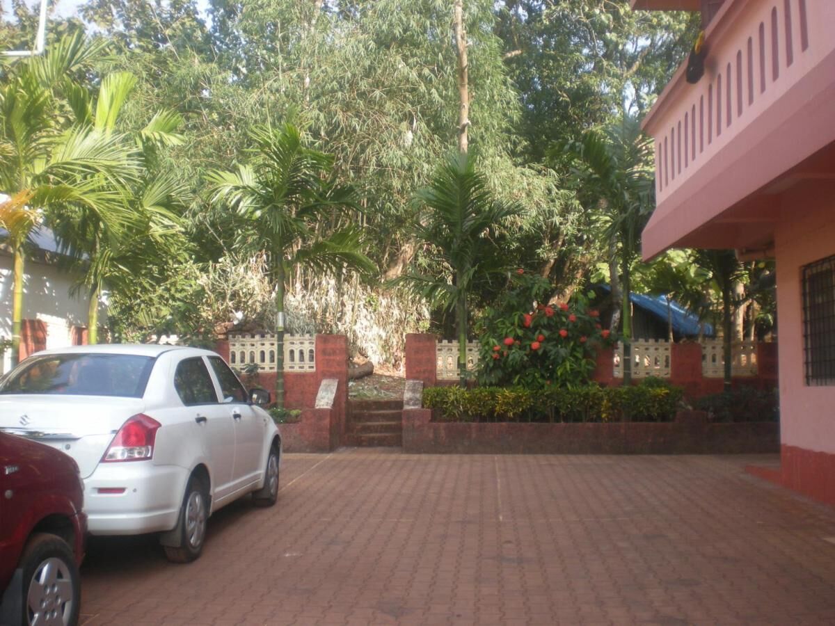 A paved driveway leading to a building with a red and white facade, surrounded by lush greenery and a parked white car.
