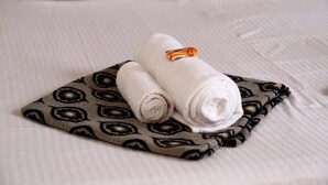 A neatly made bed with a patterned pillow and two rolled towels placed on a matching pillowcase. - Atithi Lodge (Ratnagiri)