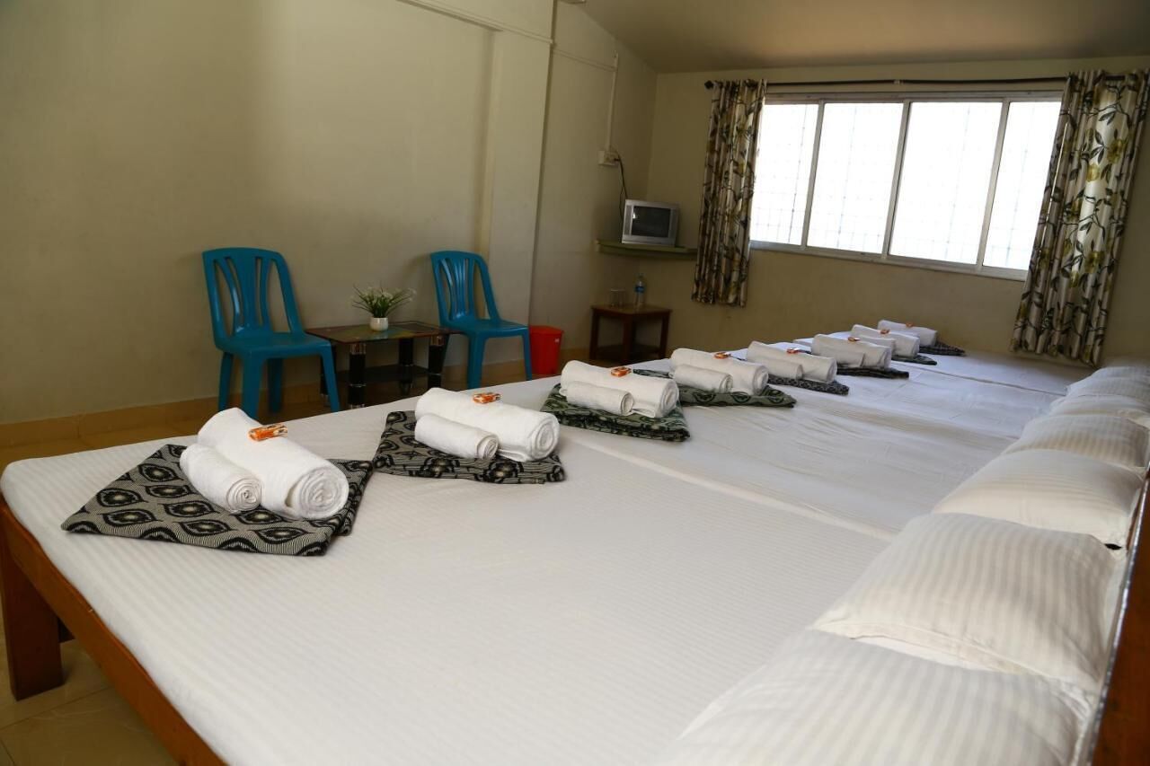 Habitación de hotel con una cama grande, dos sillas azules, una mesita con televisor y un ventanal con cortinas.