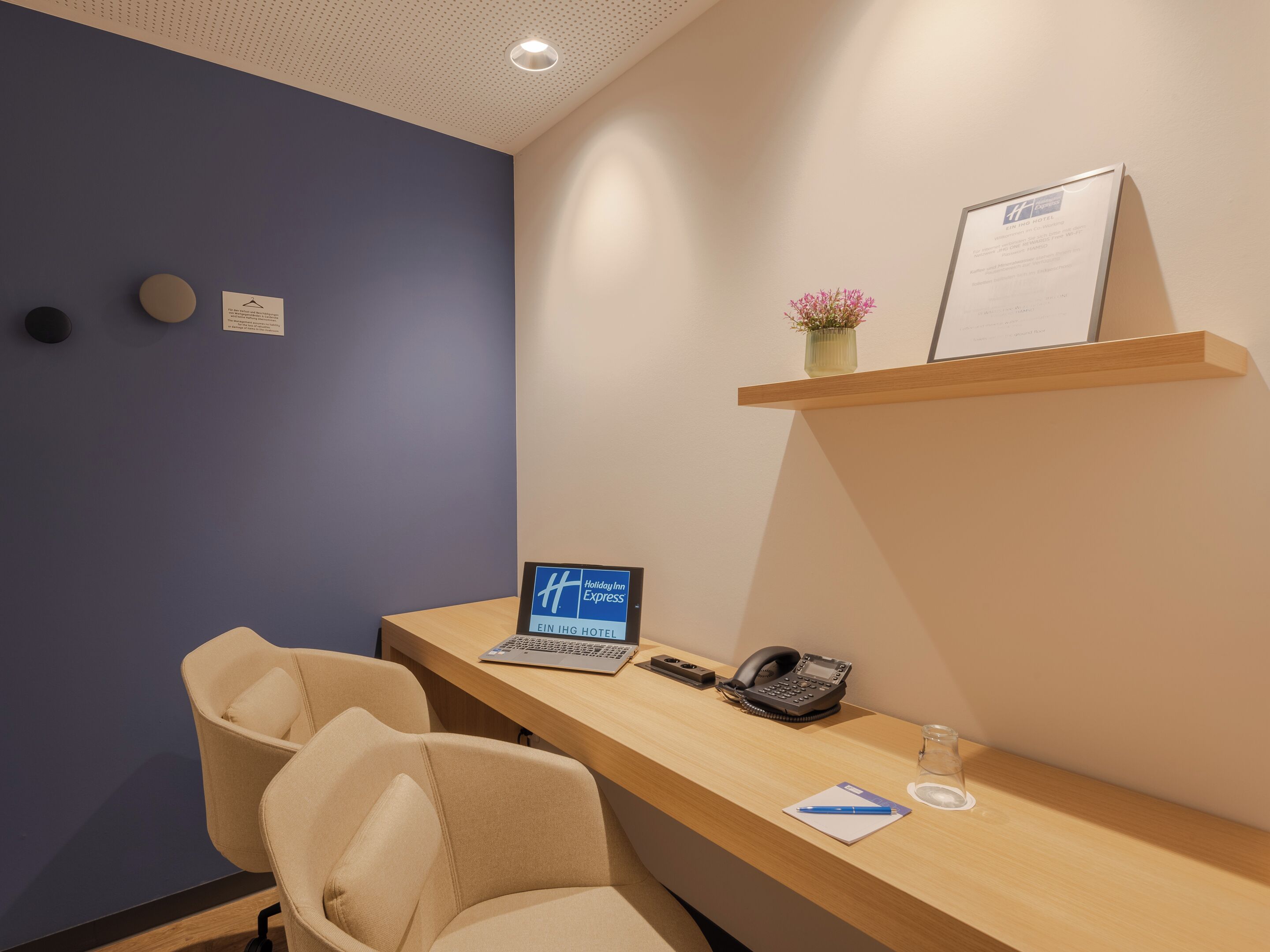 A hotel reception desk with a laptop, phone, and a small vase of flowers.