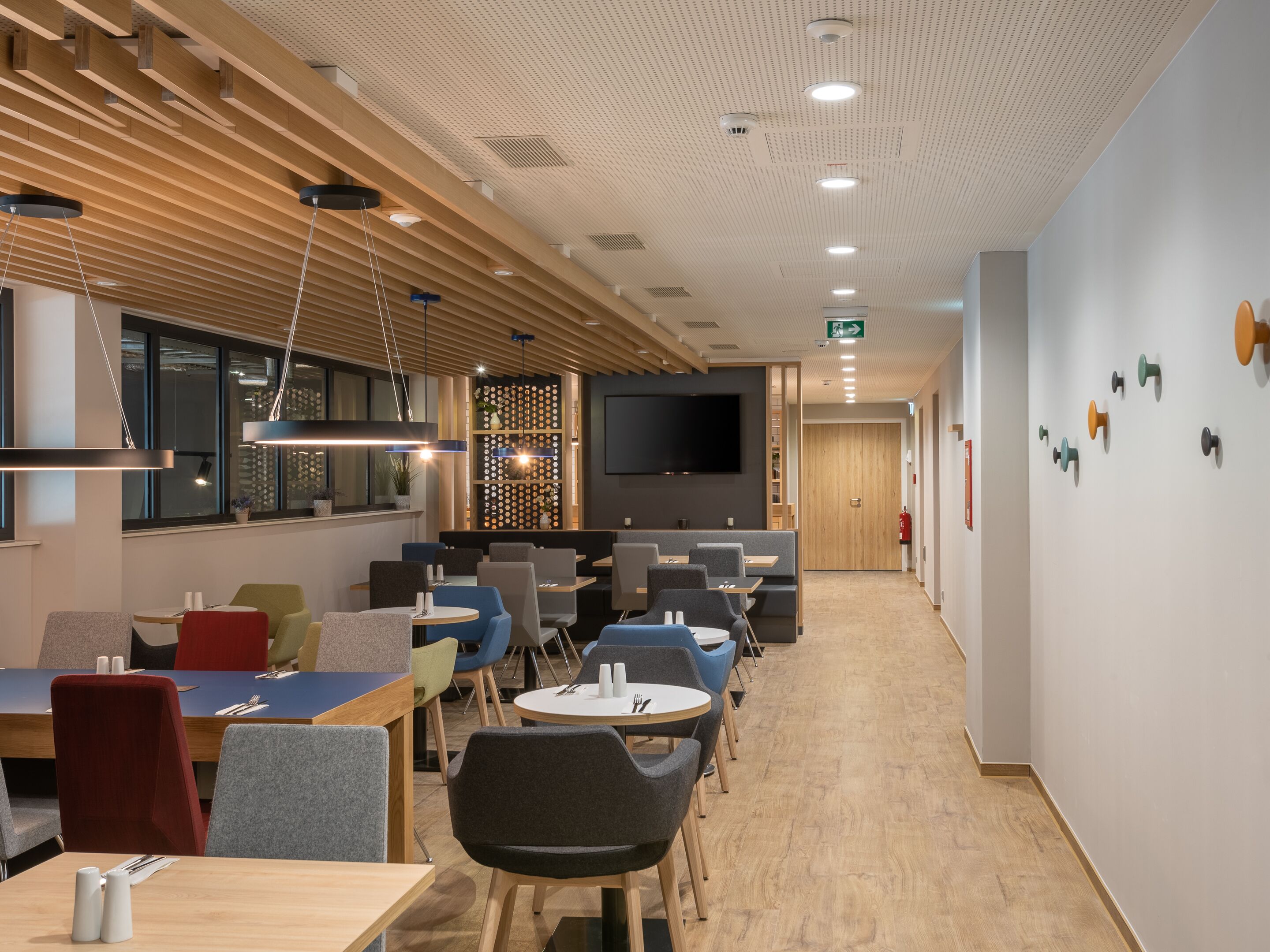 Un área de comedor moderna con vigas de madera en el techo, iluminación empotrada y diversas opciones de asientos, incluyendo mesas y sillas.