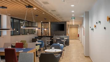 Un área de comedor moderna con vigas de madera en el techo, iluminación empotrada y diversas opciones de asientos, incluyendo mesas y sillas.