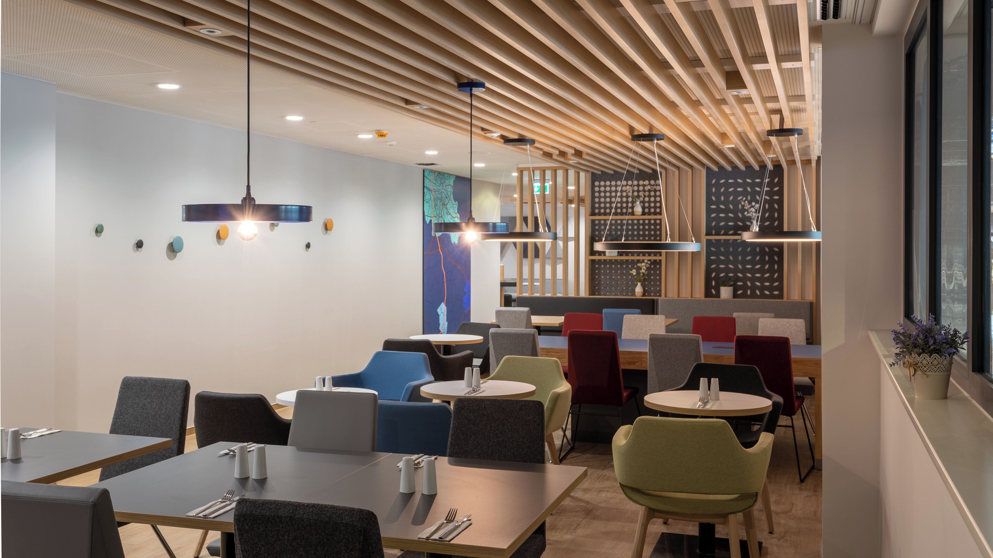 Ein modernes Restaurantinterieur mit Holzbodenpaneelen, mehreren Esstischen und Stühlen sowie Pendelleuchten.