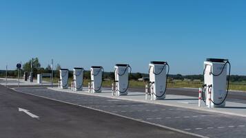 A row of electric vehicle charging stations along a road with directional signs and a clear sky.