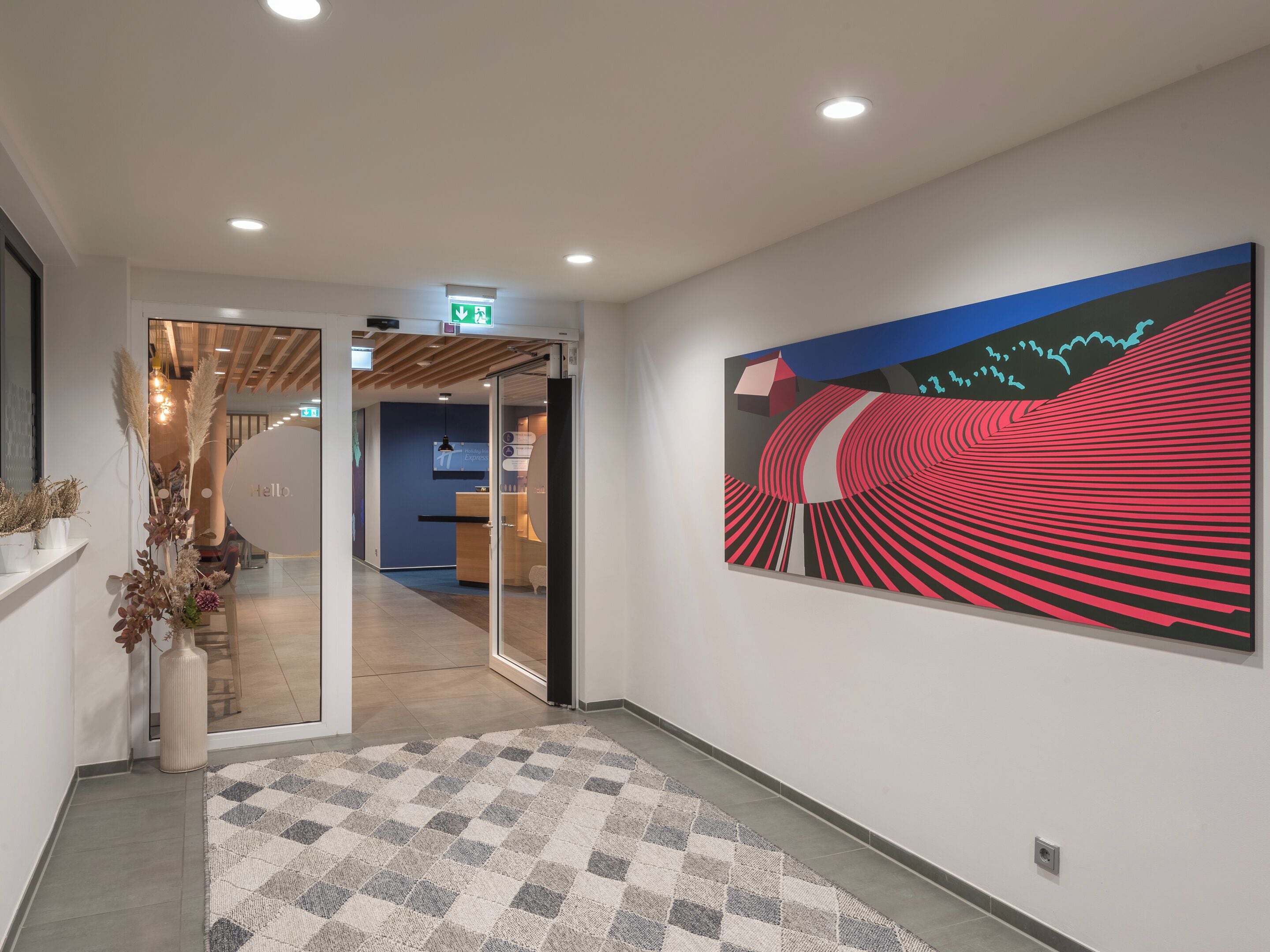 A modern hotel lobby with a checkered carpet, a reception desk, and a large abstract painting on the wall.