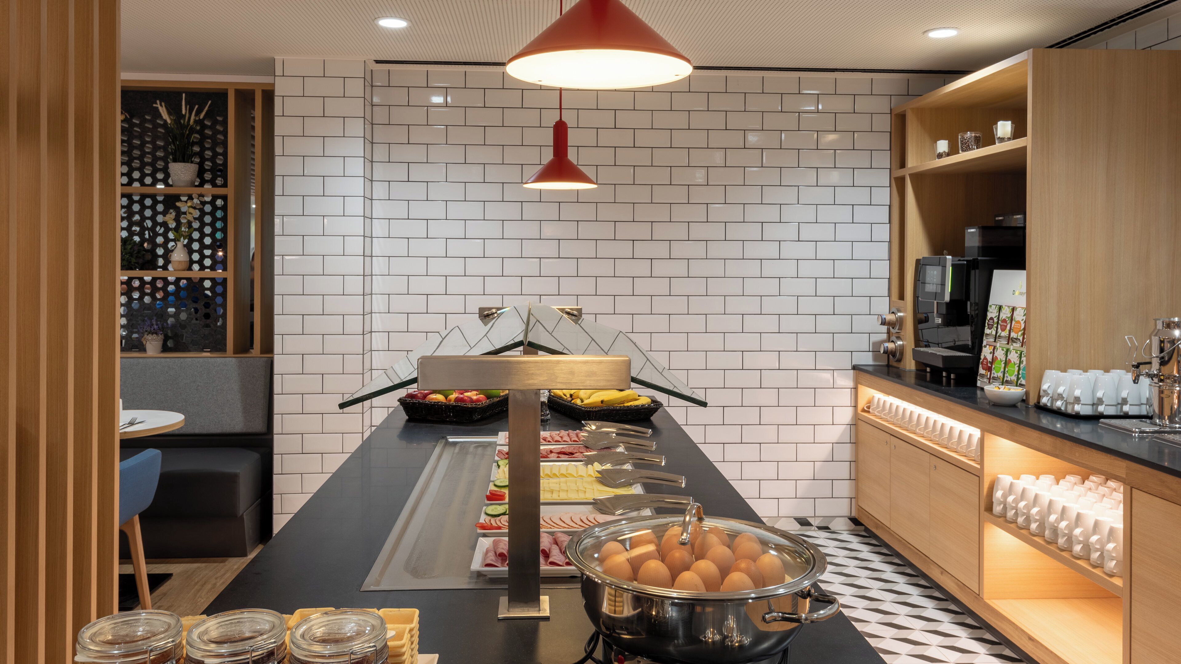 A buffet setup with various food items, a coffee machine, and a seating area with a table and chairs.