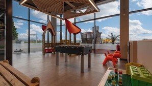 A spacious indoor play area with a foosball table, a climbing structure, and a view of the sky through large windows. - Holiday Inn Express Hamburg South A7 AS42 by IHG (Egestorf)